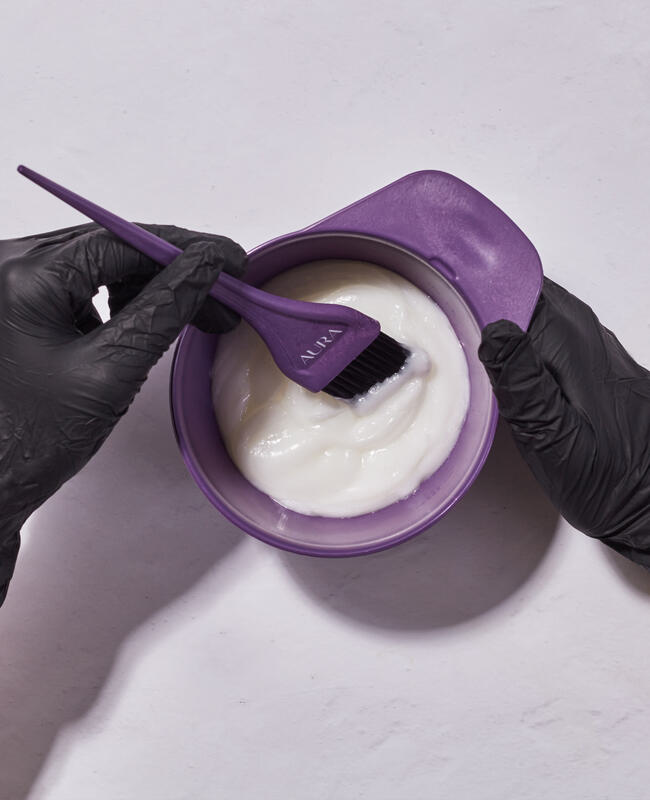 Overhead view of hair color mixing bowl with product and hair application brush on table