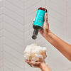 Hand squeezing AURA Body Wash onto a loofa thumbnail